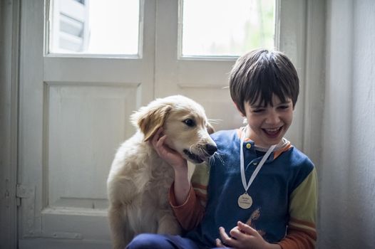 6 year old boy in pajamas with his golden retriever puppy dog in the house in front of the hall window