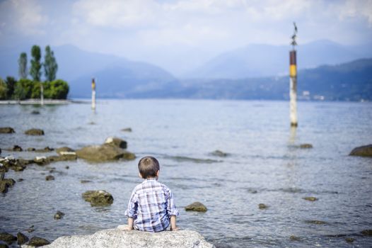 Italy, Piedmont, Isola Bella, Lago Maggiore, a child sitting on a rock looking towards infinite horizon