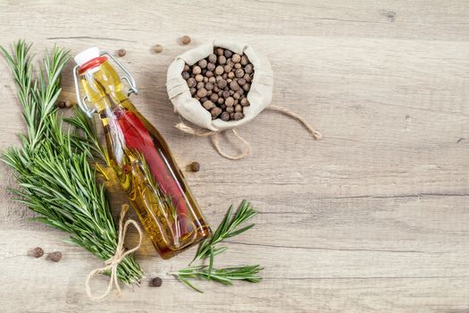 Rosemary bunch of bouquets, olive oil with pepper and spices, fragrant pepper on light wooden surface. Top view, copy space.