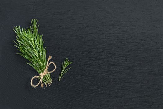 Rosemary bunch of bouquets on black stone surface. Top view, copy space.
