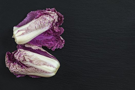 Two blue napa cabbages on black stone surface. Top view, copy space.