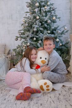 Boy and girl with bear sitting under Christmas tree