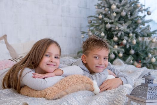 Sister and brother lying on bed under Christmas tree