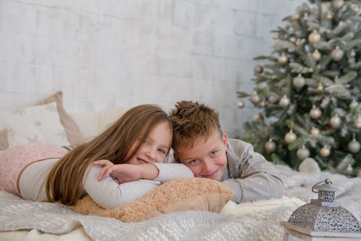Sister and brother lying on bed under Christmas tree