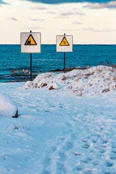 Two yellow warning signs on the winter beach