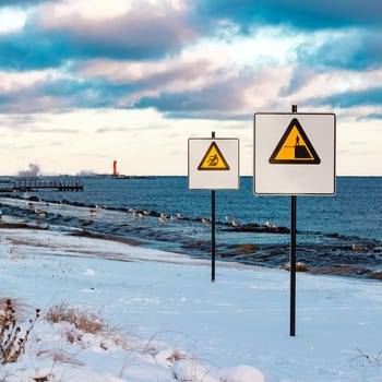 Two yellow warning signs on the winter beach