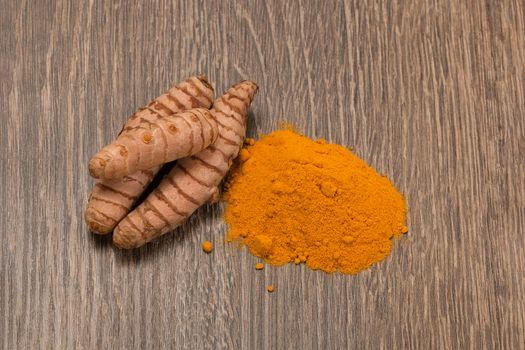 Turmeric powder with turmeric root over wood background