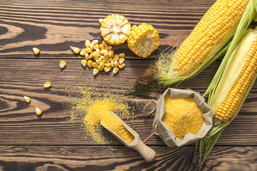 Fresh corn on cobs on rustic wooden table, top view. Dark wooden background freshly harvested organic corn. Corn grits in cloth sack.