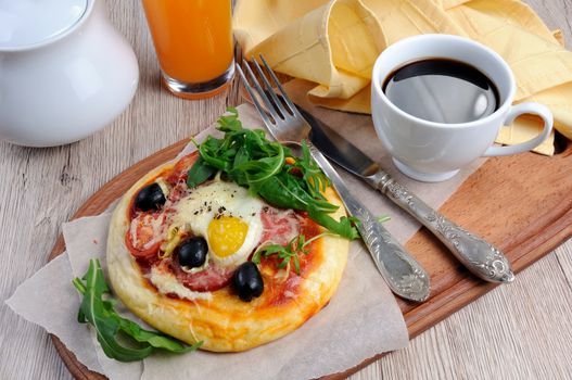 Mini pizza with sausage and egg and arugula, a cup of coffee for breakfast