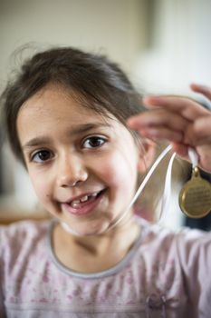 portrait of a 6 year old girl showing a medal hanging from the neck in her home