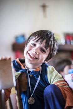 portrait of child dressed in pajamas sitting on chair at home with a medal at the neck