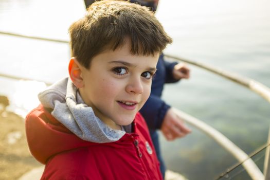 portrait of 9 year old boy with red jacket outside, as a lake background