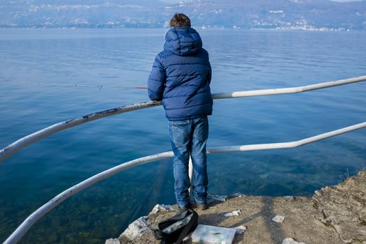 teenager on the shore of Lake Maggiore are fishing in the winter on a sunny day