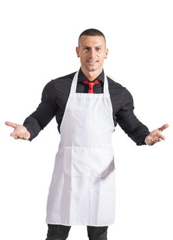Young chef or waiter posing, welcoming guests with a smile, wearing black apron and white shirt isolated on white background