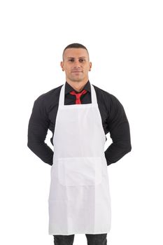 Young chef or waiter posing, welcoming guests with a smile, wearing black apron and white shirt isolated on white background
