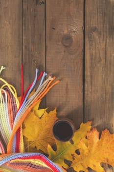 Multicolored scarf, cup of coffee, yellow maple and oak leaves on the wooden board. Bright autumn background. Sunlight, copy space, top view