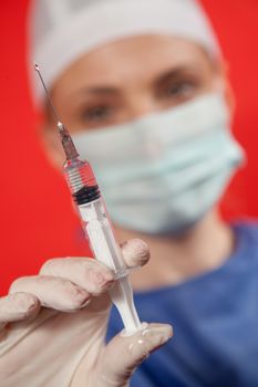 A close-up of a female doctor out of focus, holding a syringe. Red background and work path.