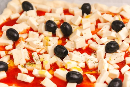 Raw pizza decorated mozzarella, black olives and tomato sauce ready to be baked