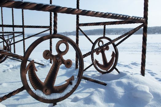 Iron sign of ancor on winter coast covered with white snow