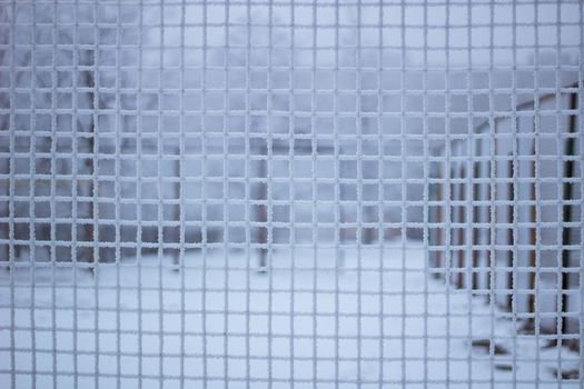 Snowed sport yard behind frosty metal grid net in winter time