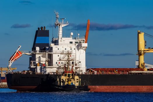 Black cargo ship mooring at the port with tug ship support