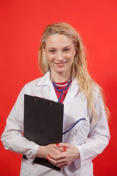 Portrait of young female doctor with white apron and folder on red background.