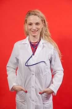 Portrait of young female doctor with white apron on red background.