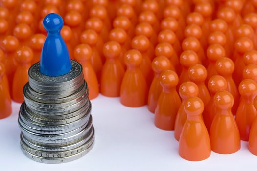 Conceptual orange game pawns as abstract view of a crowd and a blue one on a stack of money
