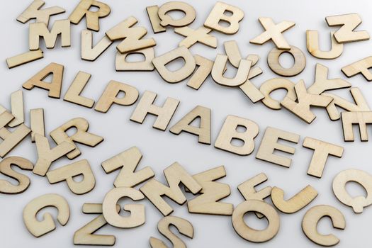 The word alphabet in wooden letters diagonally placed with loose wooden letters around it.
