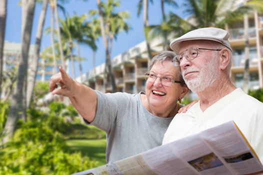 Happy Senior Adult Couple Tourists with Brochure Next To Tropical Hotel and Palm Trees.