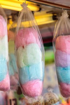 Pink, green and blue cotton candy hangs in bags at a fair