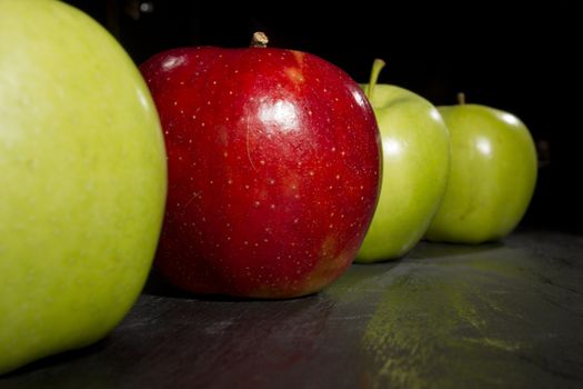 Red apple standing out in a row of green apples