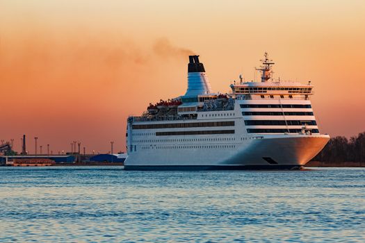 White passenger ship moving against the orange sunset sky