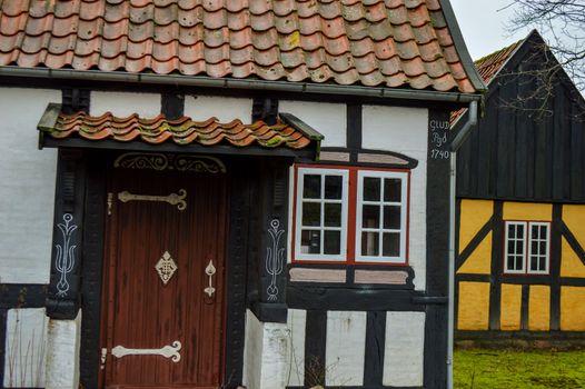A white half-timbered house with an old door and a yellow half-timbered house in the background on a cloudy day.