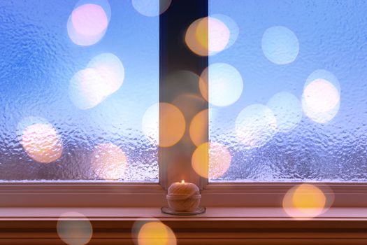 Winter composition with frosted window, burning candle and bokeh lights.