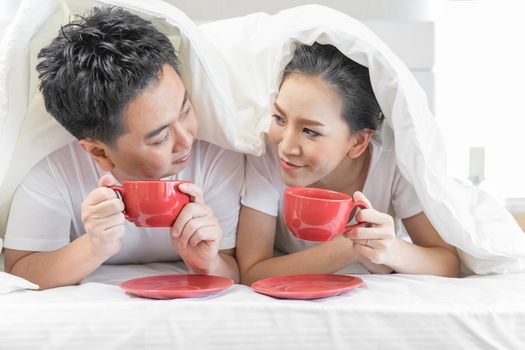 Young Asian Couples having breakfast on bed together in bedroom of contemporary house for modern lifestyle concept