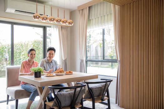 Young Asian Couples eating fried chicken together in living room of contemporary house for modern lifestyle concept