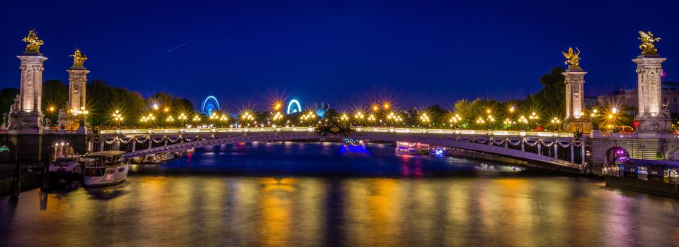 Alexander II bridge in Paris at night with big wheels in the background