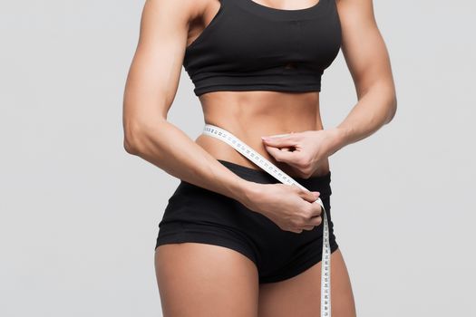 Bodybuilder girl measures the waist measuring tape on a gray background