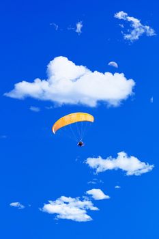 paraglider flying in a blue sunny sky with clouds