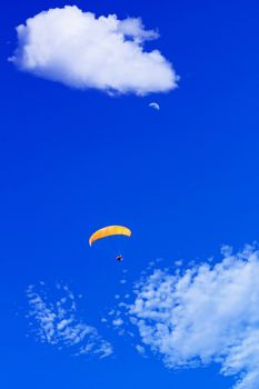 paraglider flying in a blue sunny sky with clouds