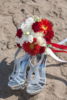 closeup of bridal shoes and wedding bouquet of flowers at the beach