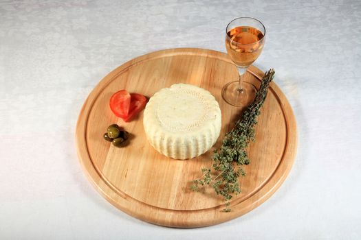 block of spicy cheese with oregano and tomato with olives on wooden plate