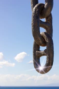 big chain with sun flair and sea with sky in the background