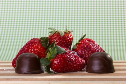 closeup of fresh strawberries and small chocolates on a wooden board