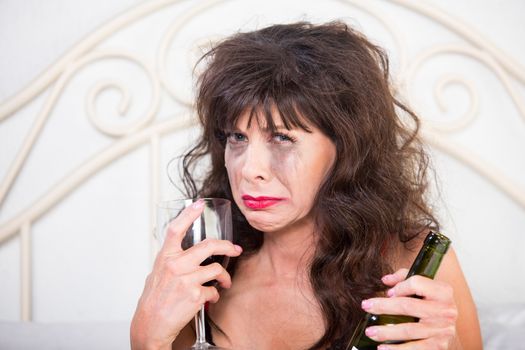 Closeup of upset mature woman crying and drinking wine in her bedroom
