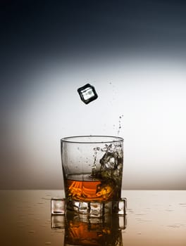 a glass of whiskey with falling ice cubes