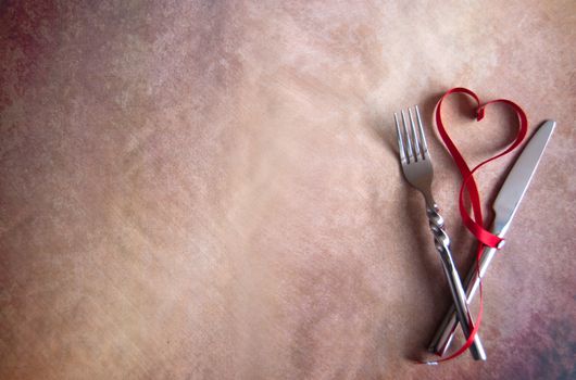 Red ribbon in the shape of a heart inbetween cutlery fork and knife