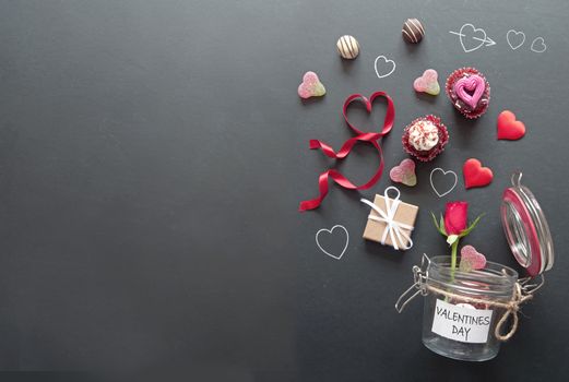 Heart, chocolates, flowers and gifts pouring out of a valentines day jar on a chalkboard