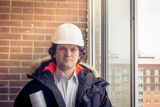 Young architect with white helmet holding blueprint and smiling look at the camera. Soft focus, toned